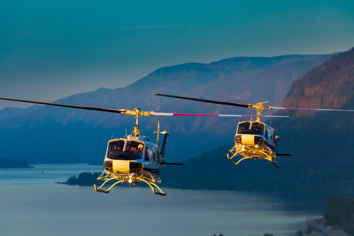 two helicopters flying over water and mountains