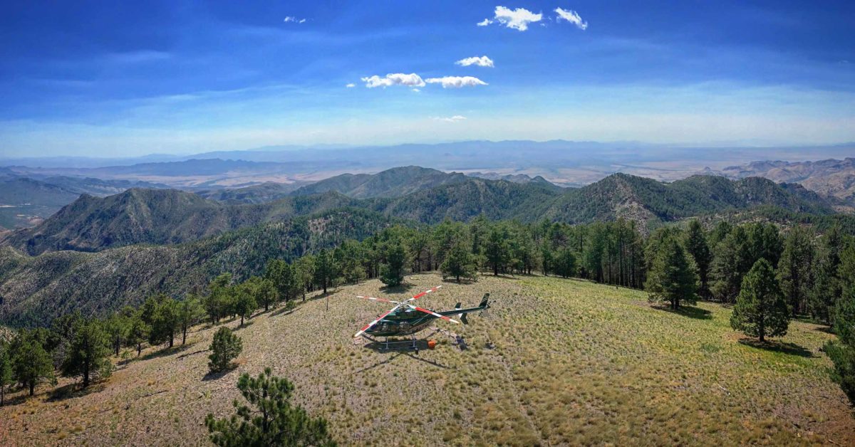 helicopter landing in a field with forested mountains in background