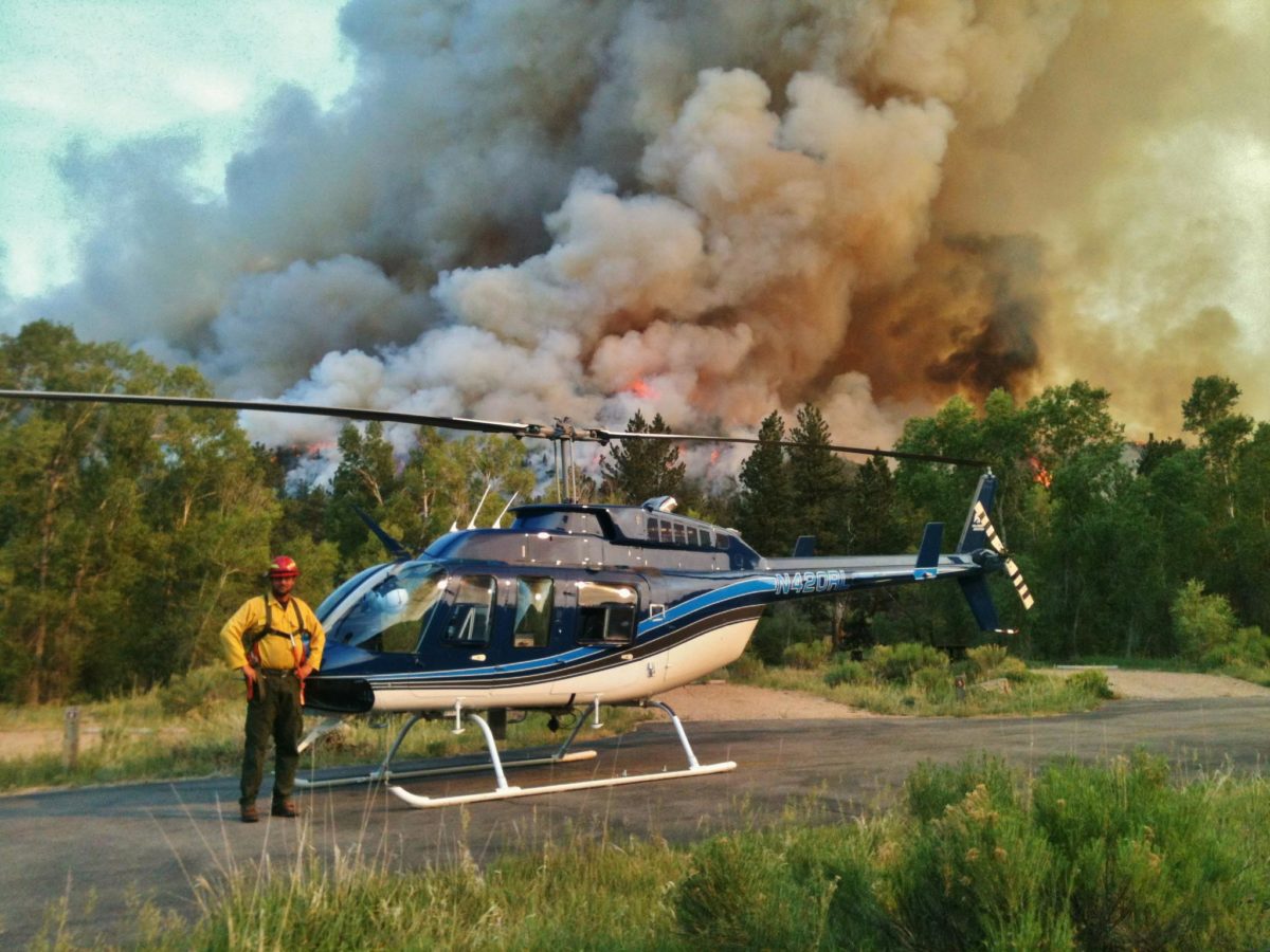 person standing with helicopter in front of billowing wildfire