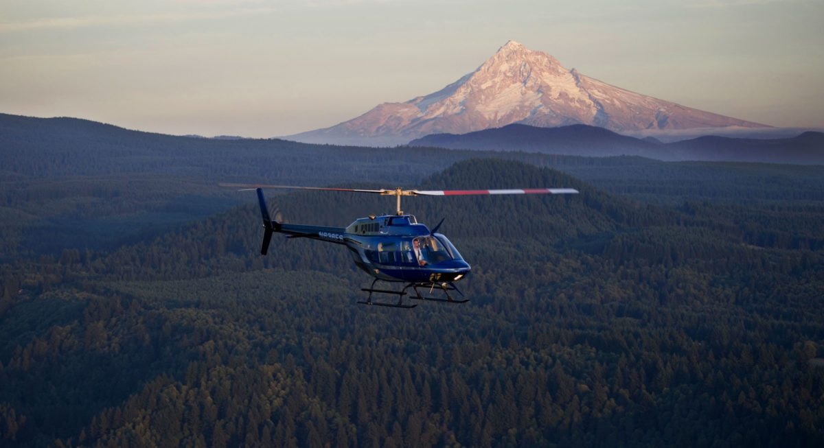 helicopter flying past mountain and forested landscape